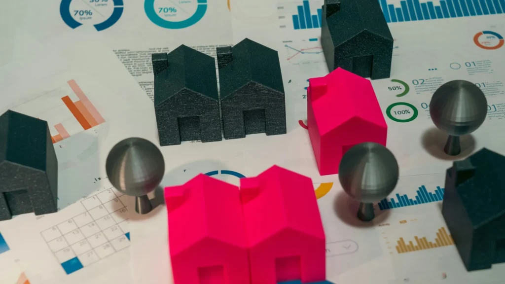 Maquetas de casas de diferentes colores sobre documentos con gráficos financieros y circulares, ilustrando el riesgo del patrimonio y el centro de intereses económicos al cambiar de residencia fiscal.