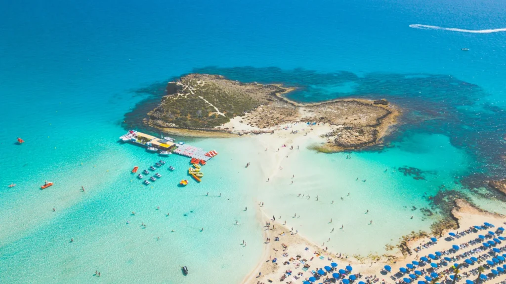 Playa y pequeña isla en Chipre con aguas mediterráneas, destino atractivo para nómadas fiscales y residencia non-dom