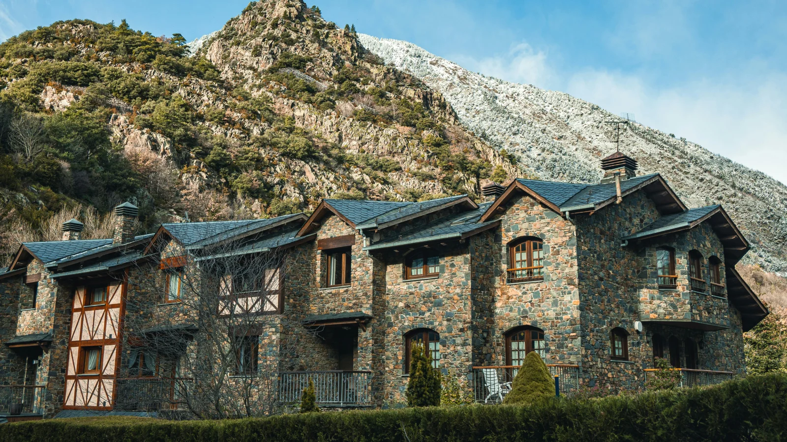 Fachada de casas tradicionales de piedra y madera en Andorra con montañas nevadas de fondo, ilustrando las opciones de vivienda para residentes fiscales.