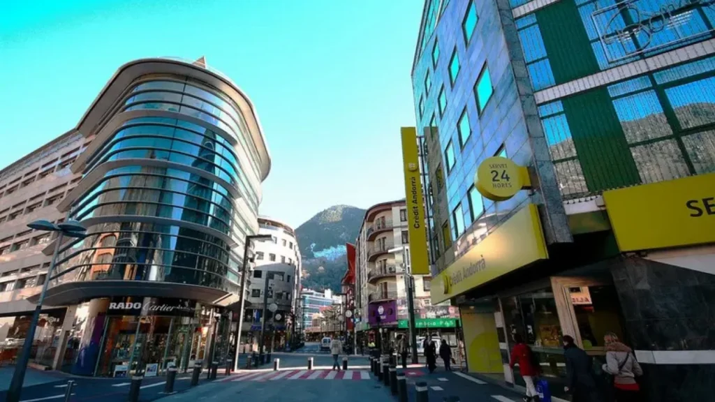 : Calle comercial en Andorra la Vella con edificios modernos y oficinas bancarias de Crèdit Andorrà, representando el entorno económico del país.