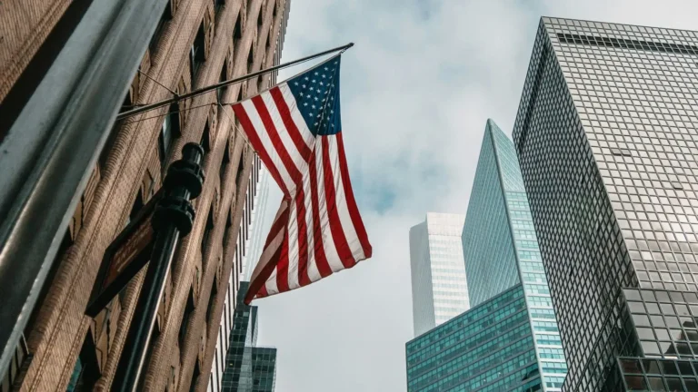 Bandera de Estados Unidos ondeando junto a grandes rascacielos corporativos, simbolizando las ventajas fiscales de una LLC para negocios digitales.