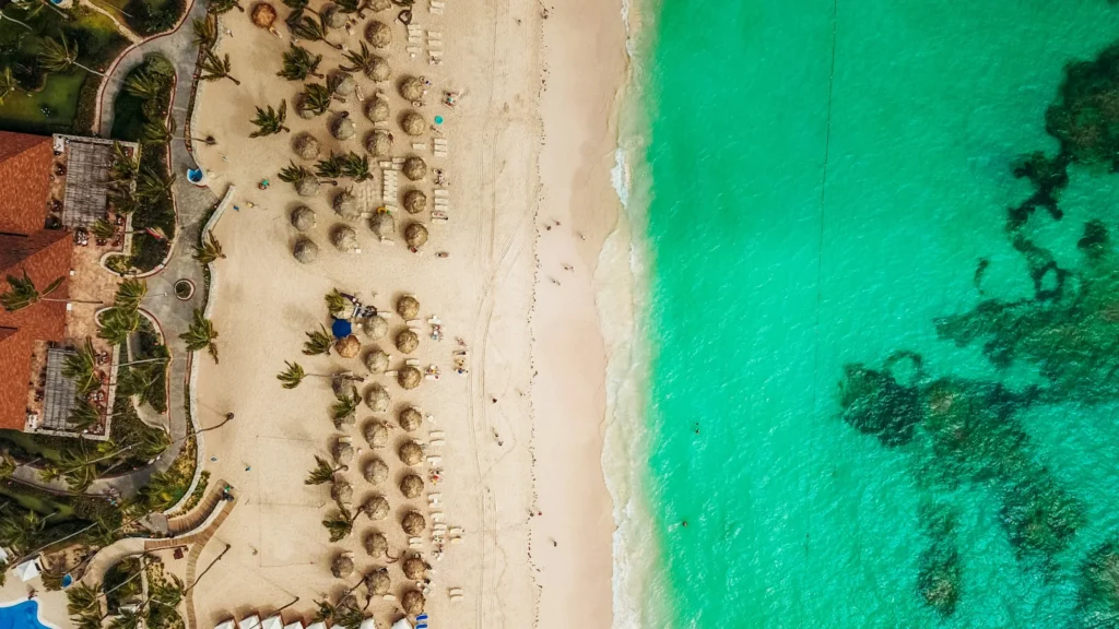 Toma cenital de un complejo turístico con sombrillas en una playa de arena blanca, ideal para inversionistas que buscan optimizar impuestos en el Caribe.
