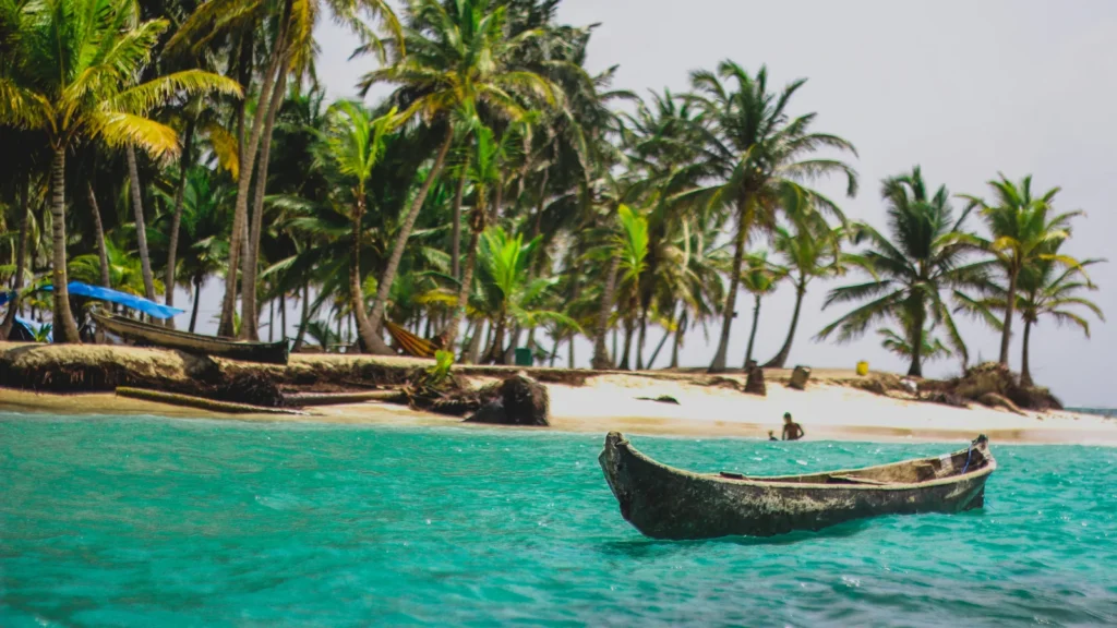 Una pequeña canoa de madera flota en las aguas turquesas de una playa tropical rodeada de palmeras en Panamá.