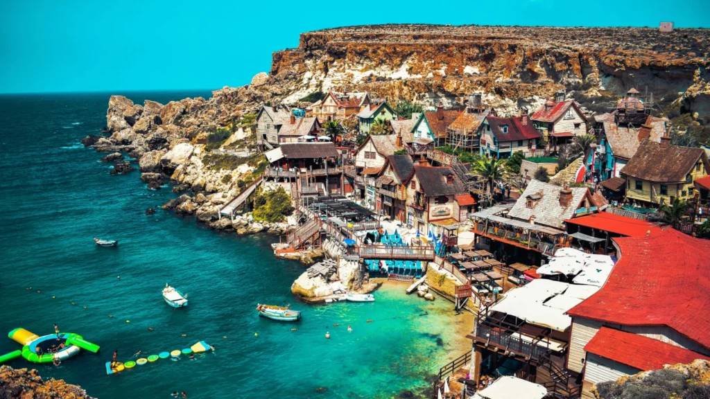 Panorámica costera de Popeye Village en Anchor Bay con aguas turquesas, reflejando la calidad de vida para inversores que abren una empresa en Malta.