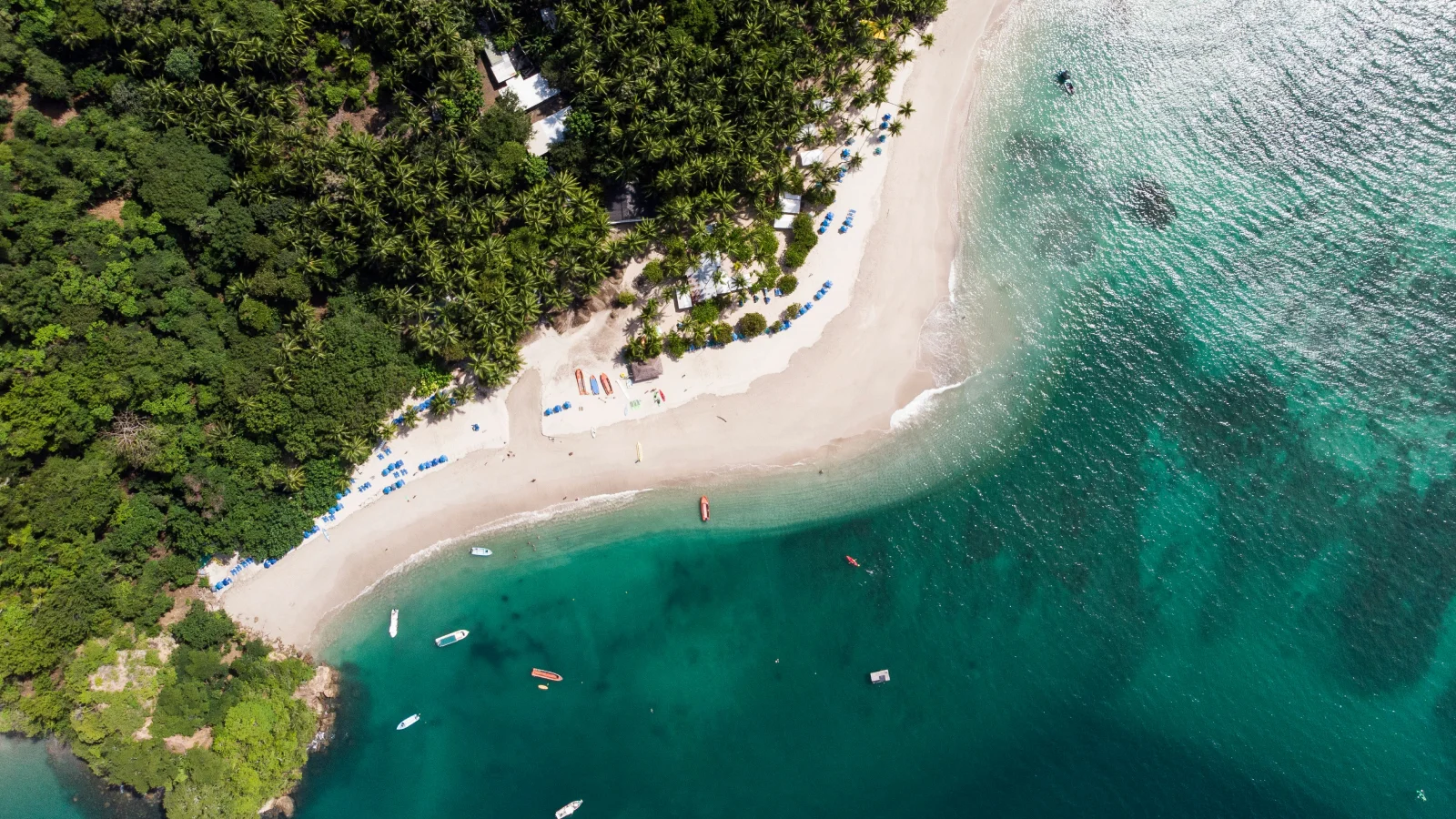 Vista cenital de una playa exótica en Costa Rica con aguas turquesas, arena clara y una densa vegetación tropical circundante.