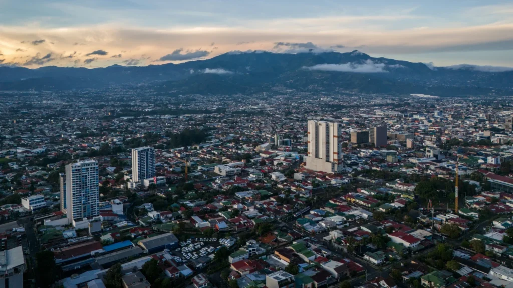 Vista aérea panorámica de la ciudad de San José, capital de Costa Rica, mostrando el desarrollo urbano y las montañas al fondo.