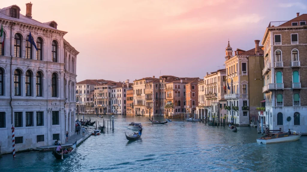 Góndolas navegando por el Gran Canal de Venecia bajo un cielo al atardecer, representando el estilo de vida en Italia.