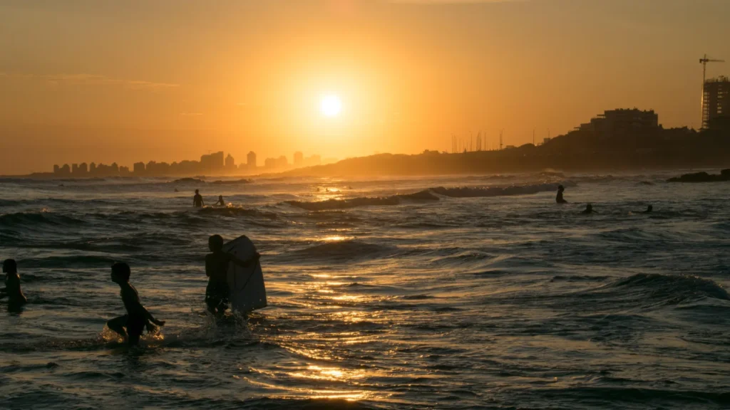Atardecer en la costa de Montevideo, Uruguay, con personas en la playa y el skyline al fondo.